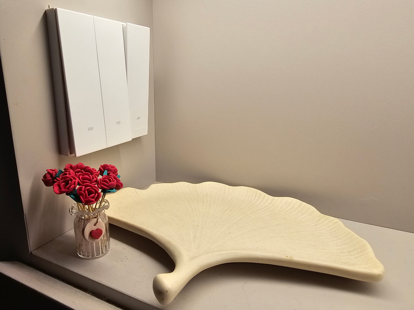 White curved bath product on a gray surface with a vase of red flowers and a mirror in the background.