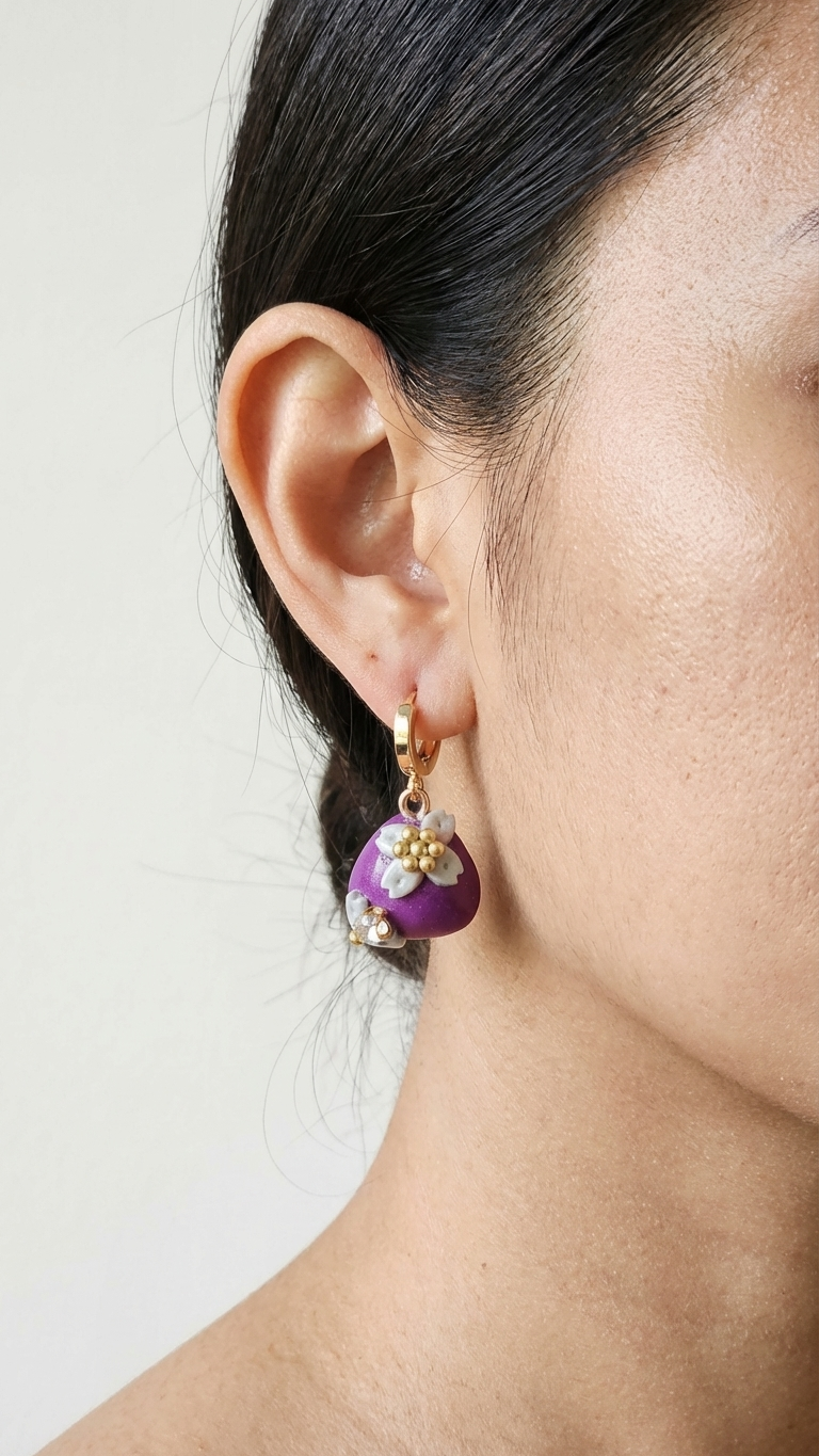 Close-up of a person wearing a purple floral earring with gold accents.