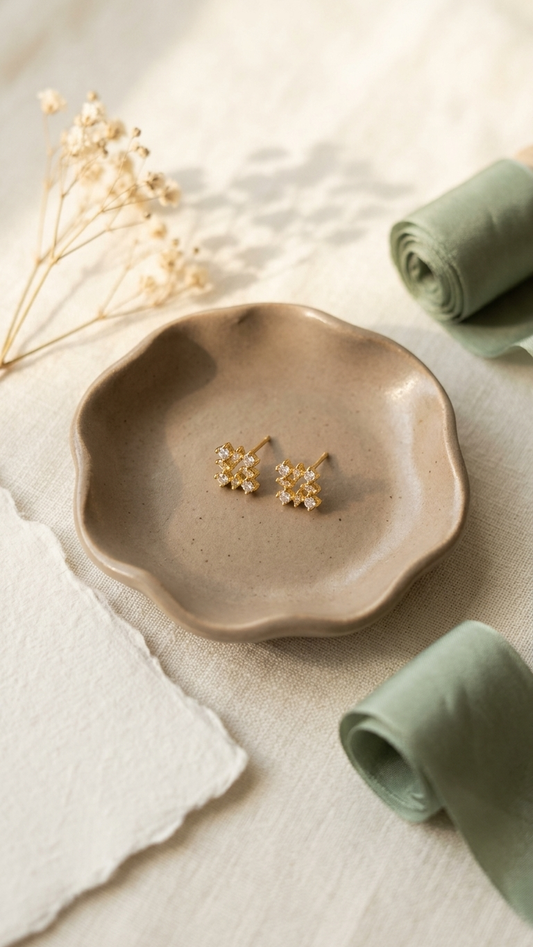 Pair of gold earrings on a beige ceramic plate with a neutral background