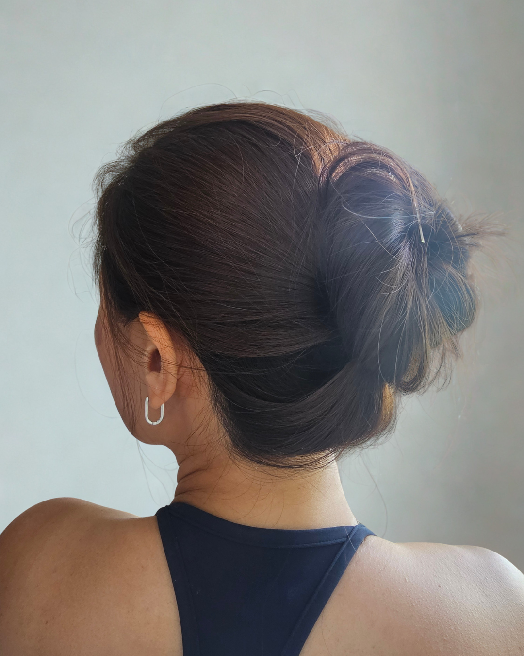 Back view of a person with a high bun hairstyle against a plain background