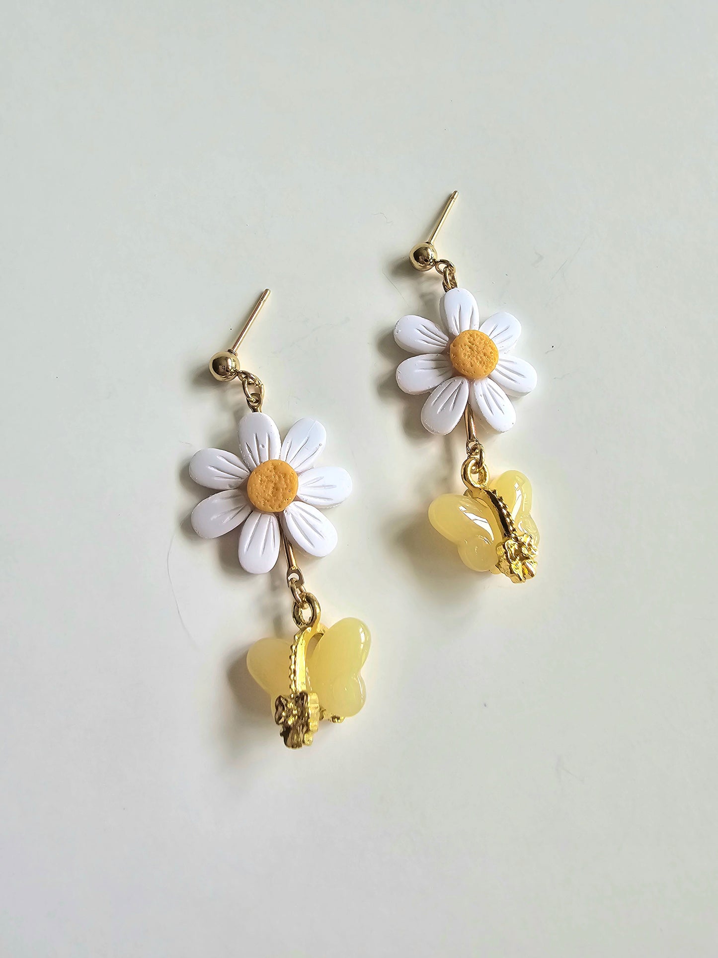 Floral earrings with daisy flowers and yellow heart charms on a light gray background