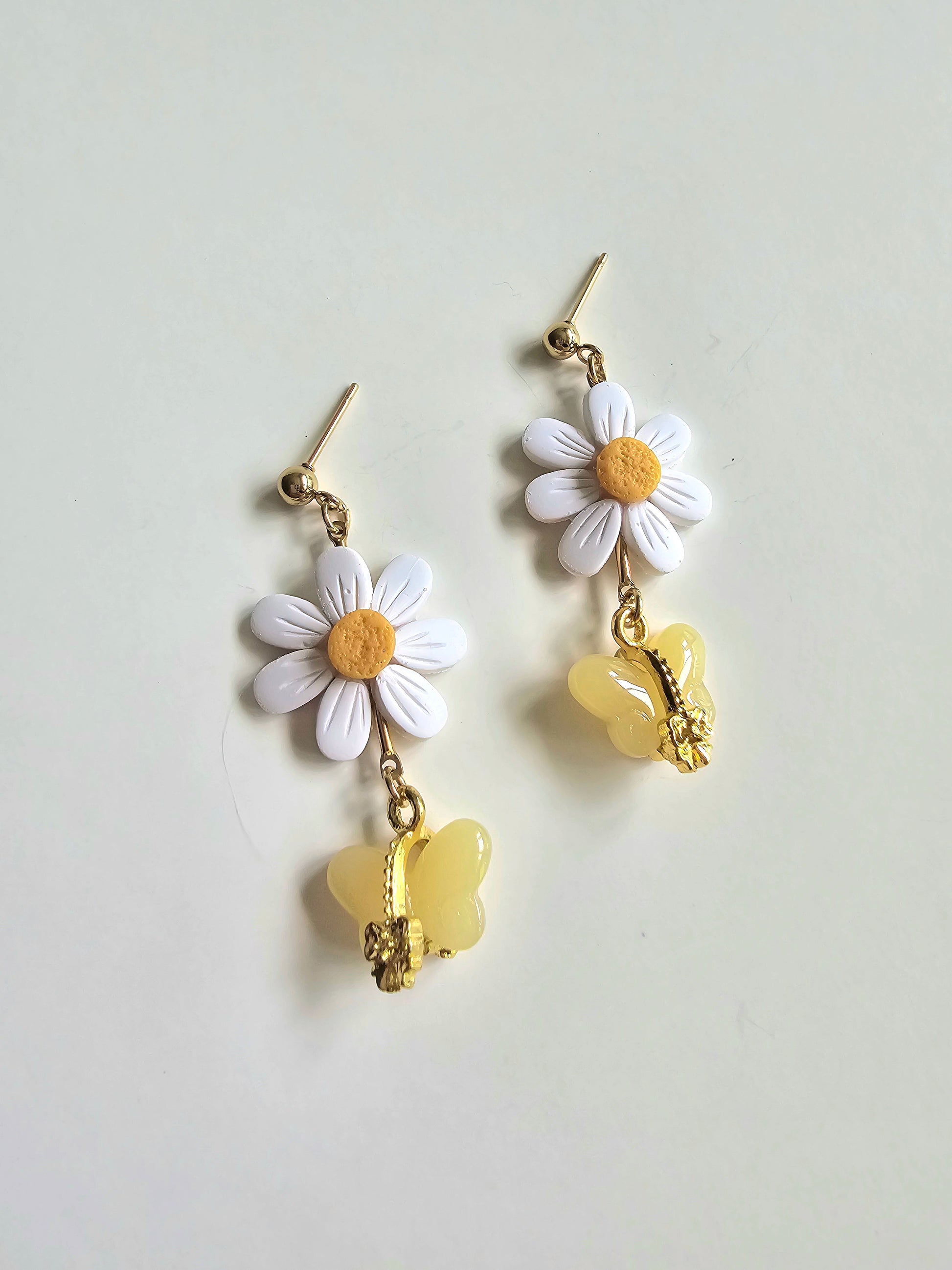 Floral earrings with daisy flowers and yellow heart charms on a light gray background