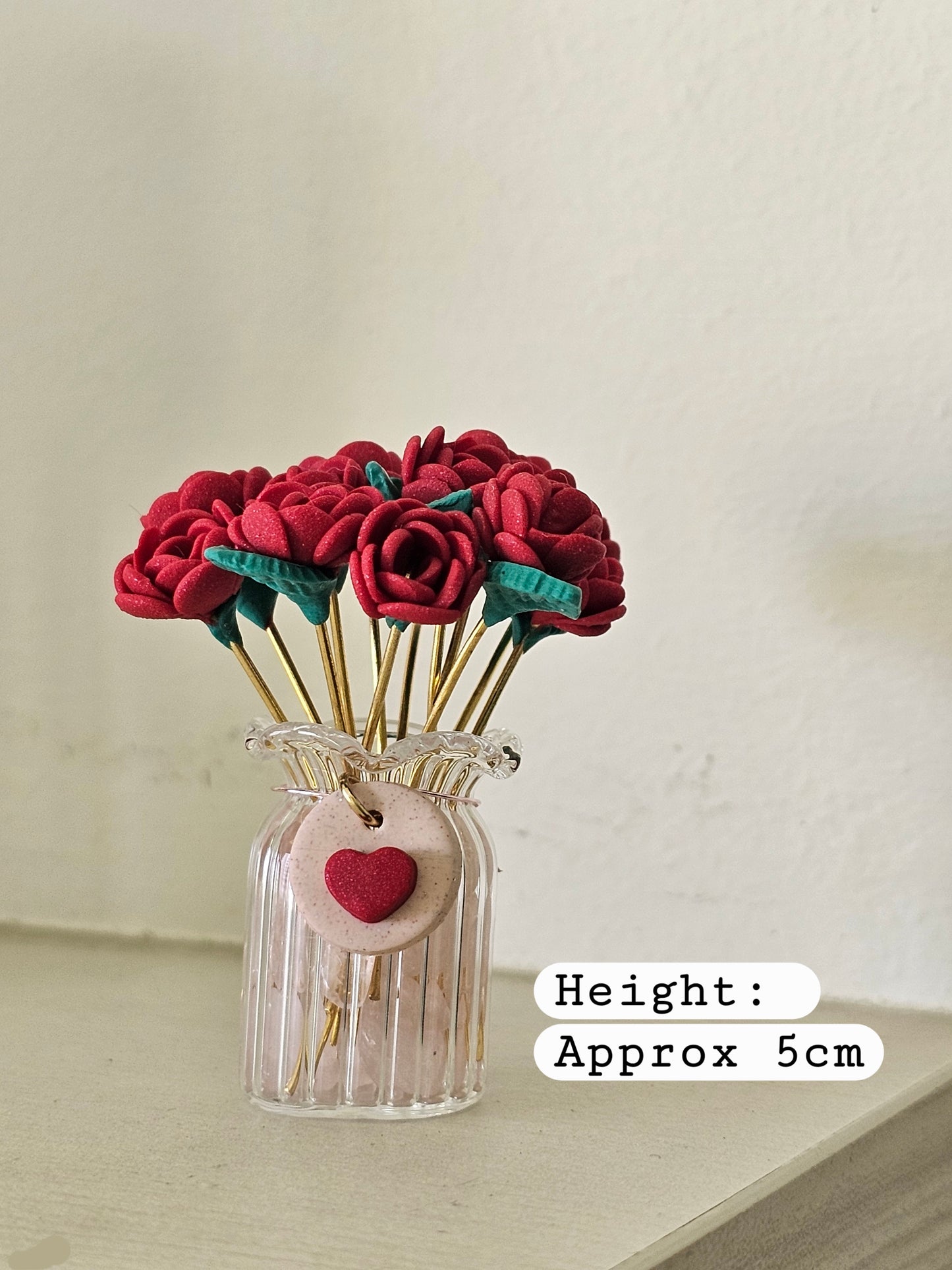Small glass vase with red fabric flowers and a heart tag on a light background
