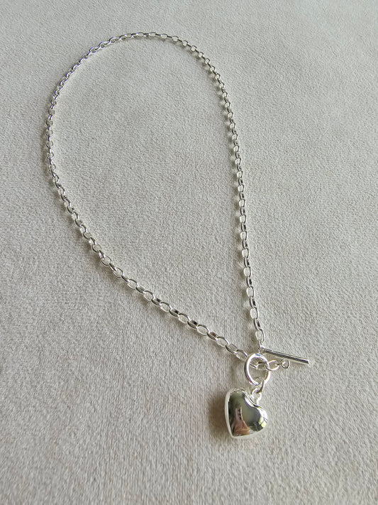 Silver chain bracelet with a heart-shaped charm on a light gray background