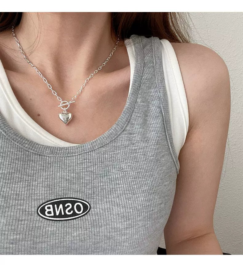 Person wearing a silver necklace with a heart pendant, gray tank top with 'OSNB' logo, and white shirt underneath.
