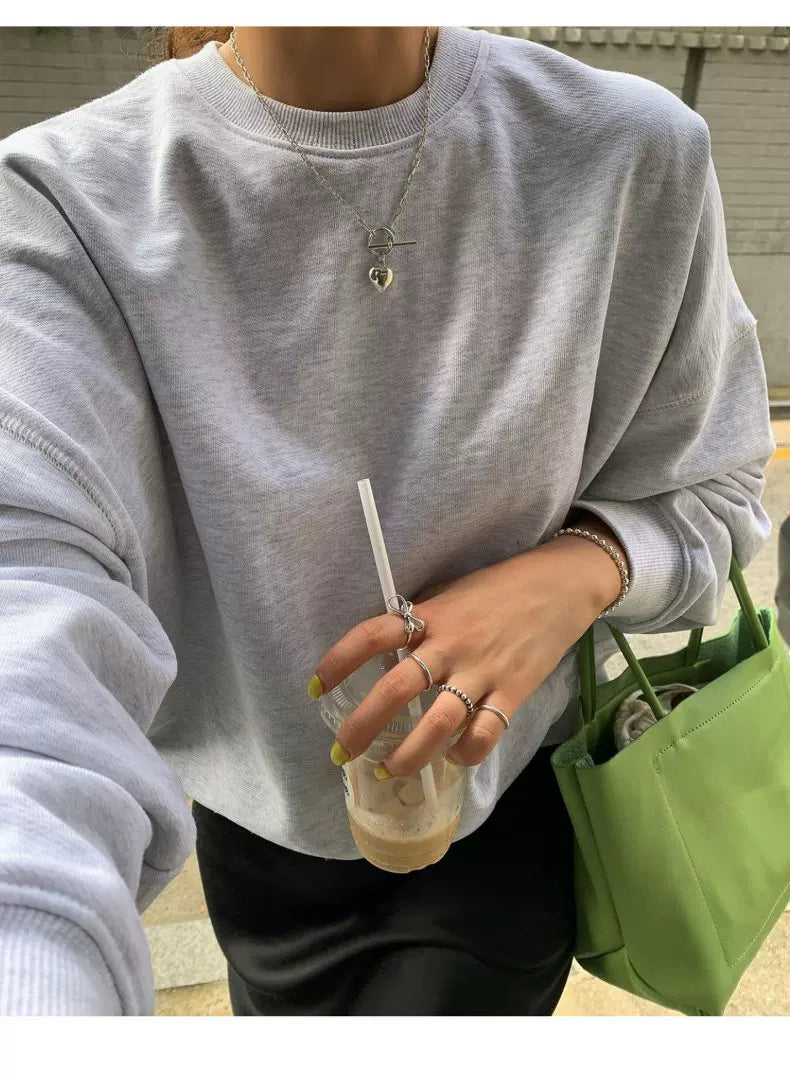 Person wearing a gray sweatshirt holding a drink with a straw and a green bag.