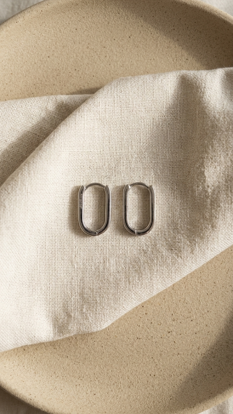 Pair of silver earrings on a beige fabric surface