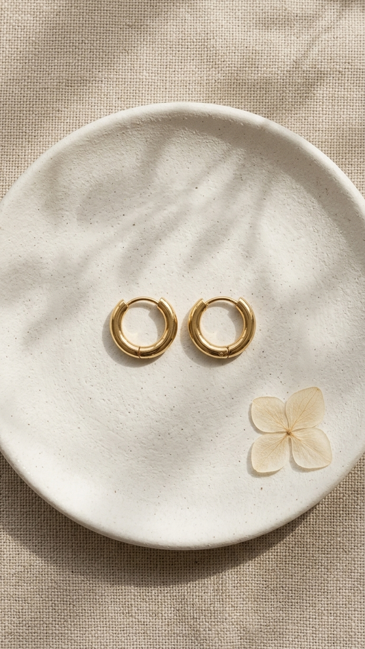 Gold hoop earrings on a white ceramic dish with a dried flower petal.