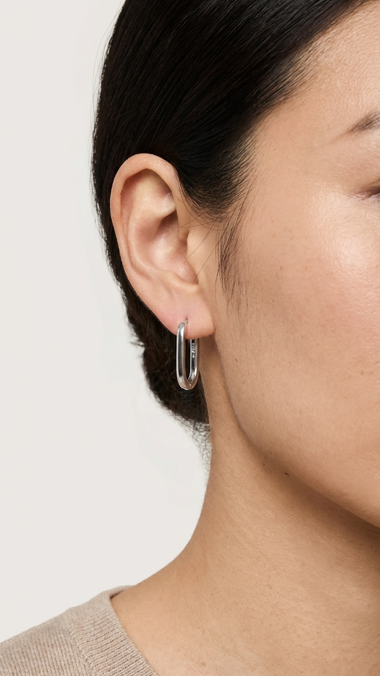 Close-up of a person wearing a silver hoop earring on a plain background