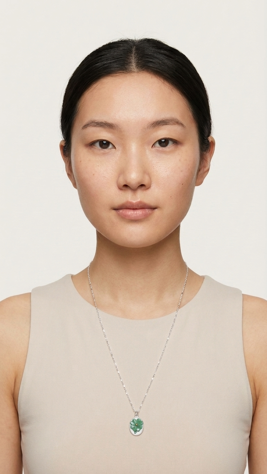 Woman wearing a necklace with a green pendant against a plain background