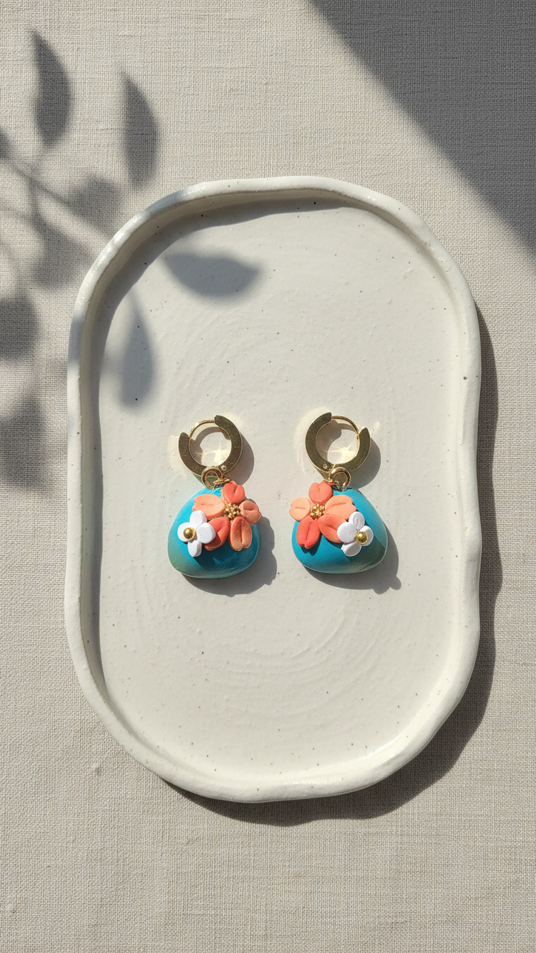 Pair of turquoise earrings with floral designs on a white dish.