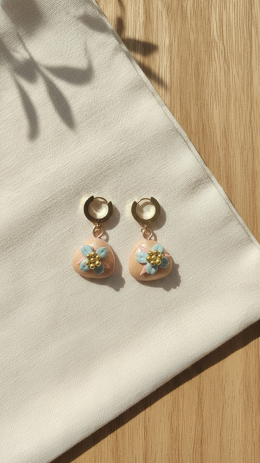 Pair of earrings with floral designs on a beige fabric background