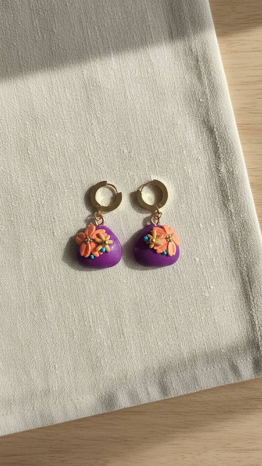 Purple heart-shaped earrings with floral designs on a light fabric background