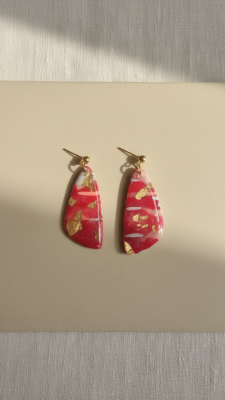 Pair of red earrings with gold accents on a beige surface