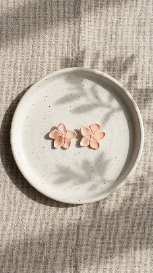 Pink flower-shaped earrings on a white plate with a beige background