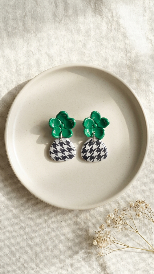 Pair of earrings with green floral tops and black and white checkered bases on a beige plate.