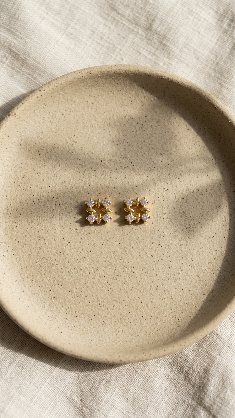 Pair of gold earrings on a beige ceramic plate with a neutral background