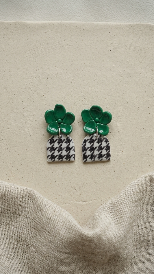 Pair of earrings with green tops and checkered bottoms on a beige fabric background