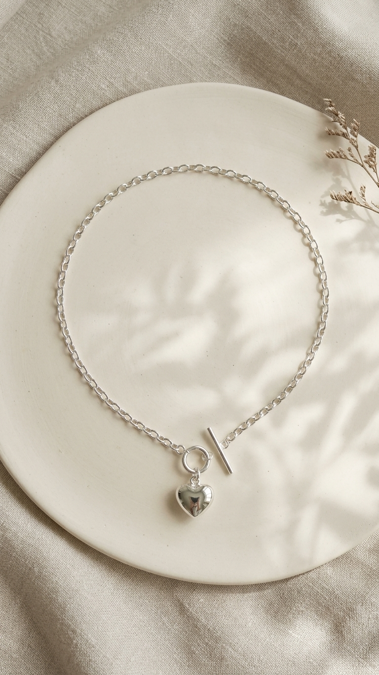 Silver bracelet with a heart charm on a beige plate