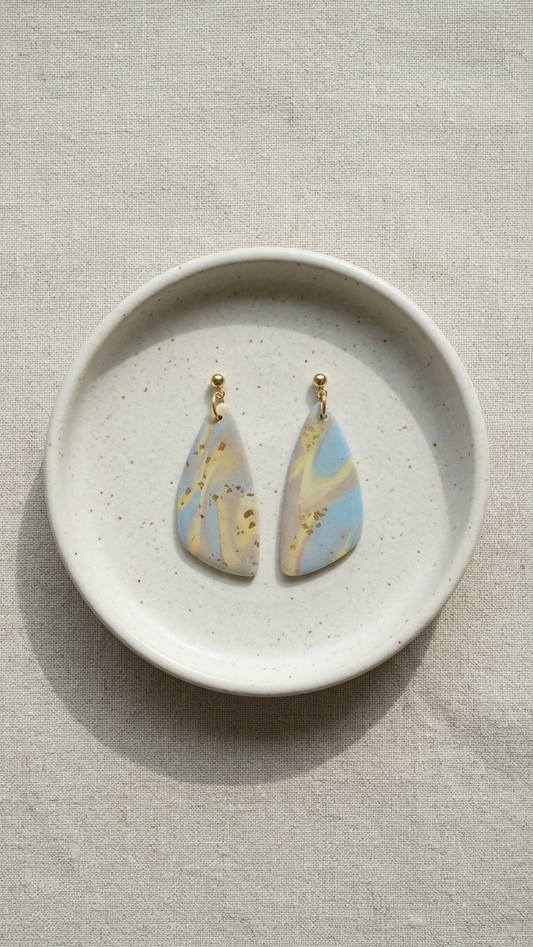 Pair of earrings on a textured ceramic dish with a neutral background
