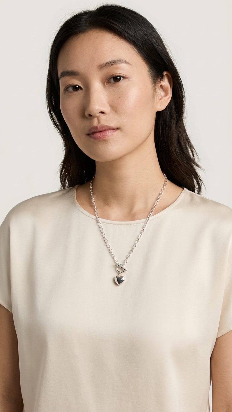 Woman wearing a necklace with a heart pendant against a plain background