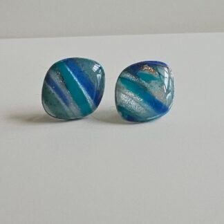 Pair of small square blue marbled polymer clay stud earrings with stainless steel posts, featuring teal, navy, grey tones, and subtle shimmer on a light background.