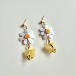 Handmade white daisy polymer clay earrings with yellow butterfly charm and gold-plated stainless steel post, photographed on a neutral background.