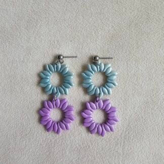 Two-tone polymer clay petal wreath earrings in sky blue and lilac with stainless steel posts, photographed on a neutral fabric background