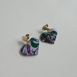 Handcrafted polymer clay heart-shaped earrings with green and purple marbled patterns and gold-plated hexagonal posts on a neutral background
