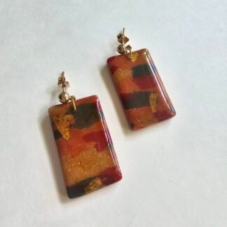 Handcrafted polymer clay rectangular drop earrings in amber and rust tones with gold foil accents on a neutral background