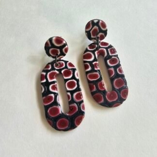 Handcrafted polymer clay oval drop earrings with crimson abstract pattern and stainless steel studs on a neutral background