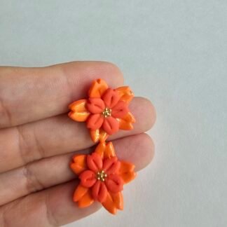 Handcrafted polymer clay coral and orange floral stud earrings with layered petals on a light background