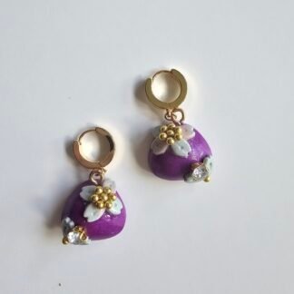 Gold plated huggie earrings with violet polymer clay puff charms, pale blue floral details, and crystal accents on a white background
