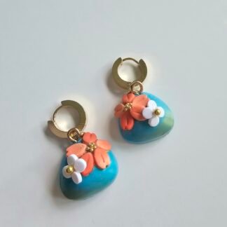 Gold plated huggie earrings featuring ocean blue polymer clay puff charms with coral and white floral details on a white background