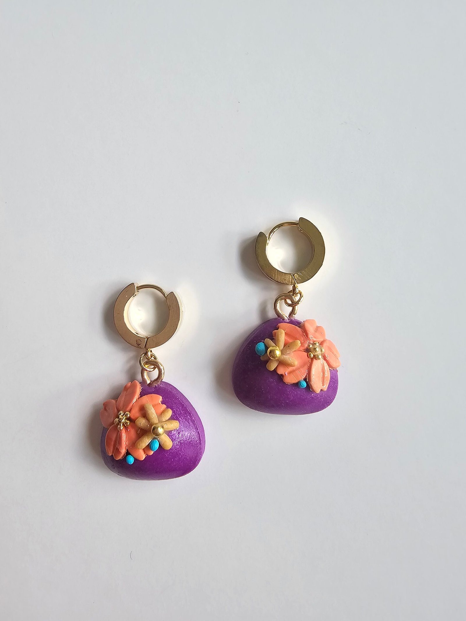 Gold plated huggie earrings with violet polymer clay puff charms and peach floral details on a white background
