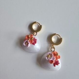 Gold plated huggie earrings with pearly white polymer clay puff charms decorated with pastel floral details on a white background