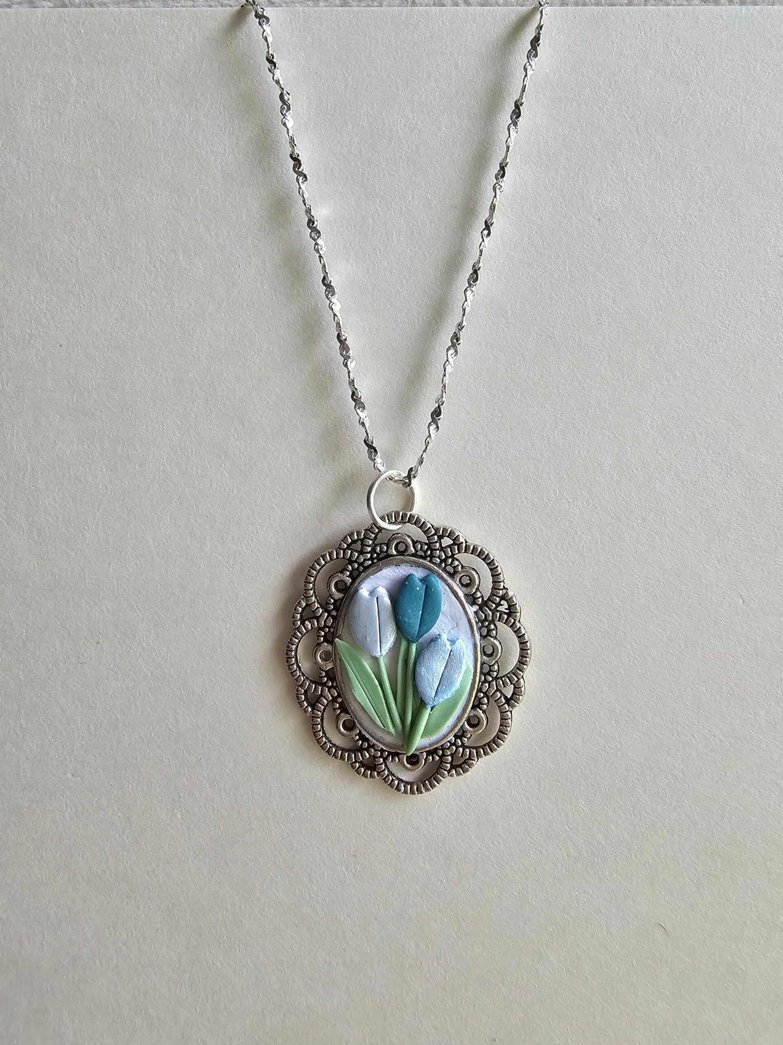 Handcrafted polymer clay floral pendant necklace in pastel blue and green, set in an ornate silver oval frame, on a 925 sterling silver chain by Haeng Bok Clay