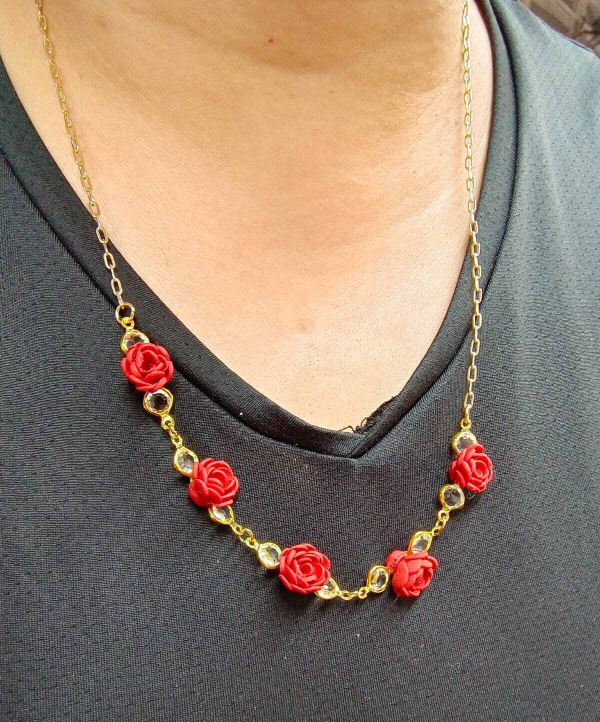 Custom handcrafted necklace featuring red polymer clay rose charms accented with clear crystal details on a gold-toned chain, worn around the neck against a black top.