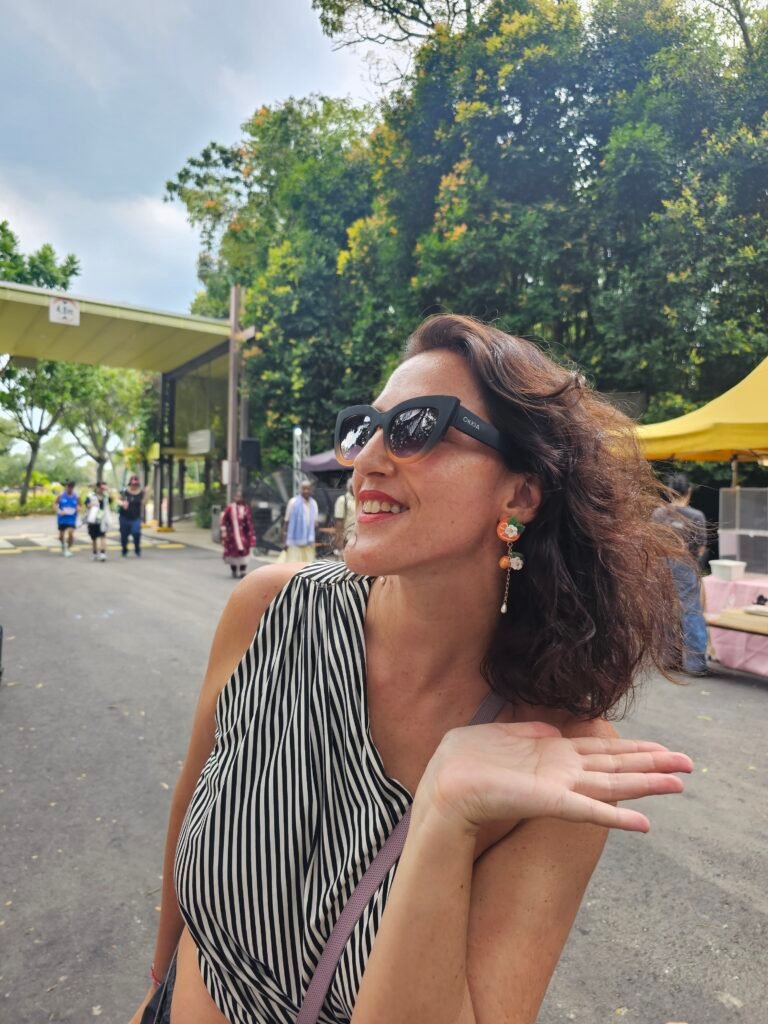 Customer wearing Haeng Bok Clay orange floral polymer clay earrings at Sentosa Festive Market, photographed outdoors with greenery and market stalls in the background.